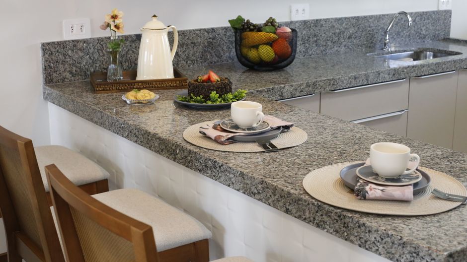 Kitchen counter with cups and a plate set out on a stone surface.